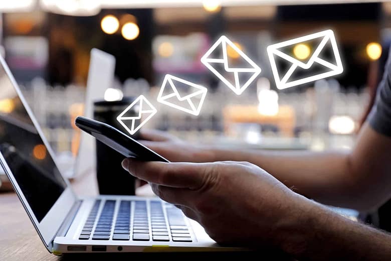 Hotel email marketing - person sending emails from smartphone with laptop, representing AGR's hotel email marketing services for new guest acquisition