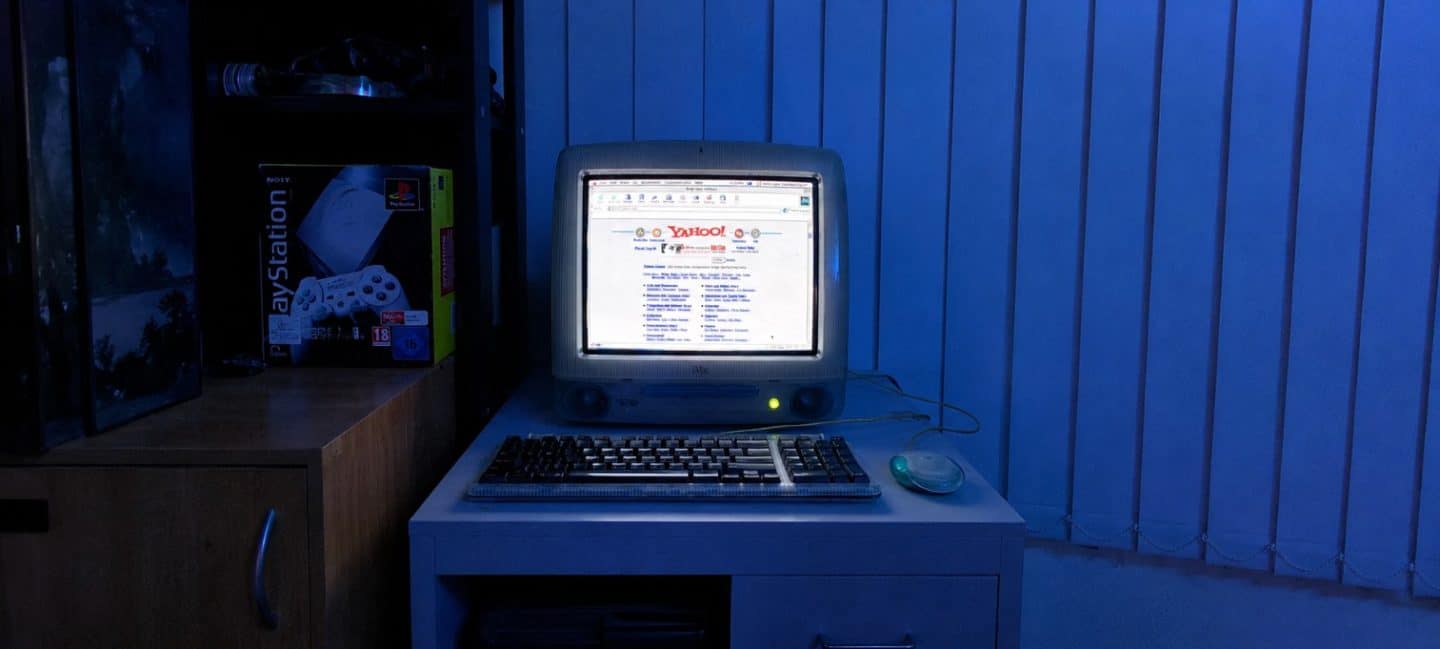 A late 1990s iMac displaying Yahoo on screen with a PlayStation box visible in the background, representing the early internet era when Americas Great Resorts published its 1998 warning about OTA dependency in luxury hospitality.