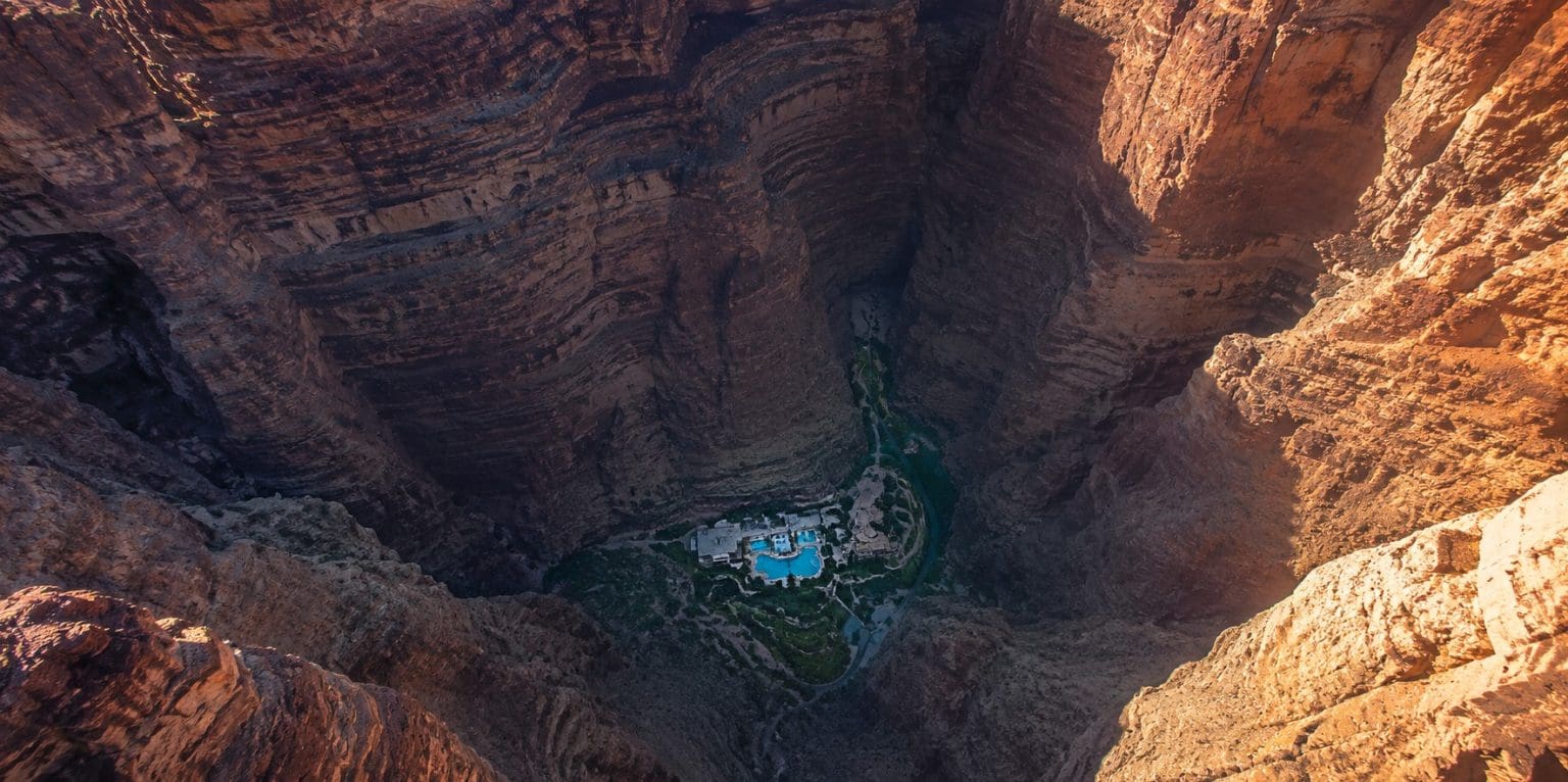 A luxury resort at the bottom of a deep canyon, dwarfed by layered rock walls rising on all sides, seen from above.