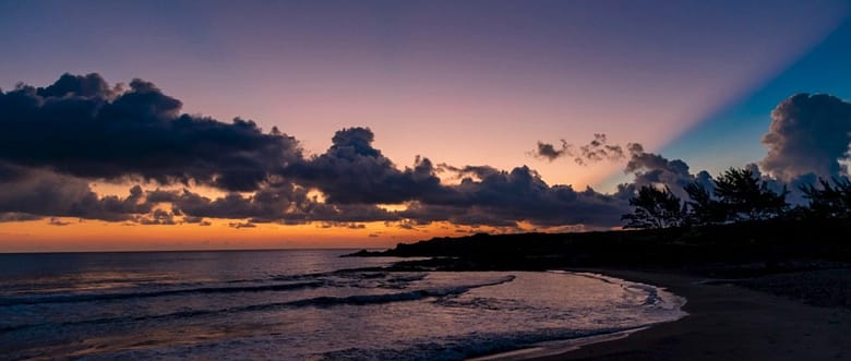 Oceanfront luxury hotel setting at twilight, an orange horizon glow over the ocean beneath a deep blue sky