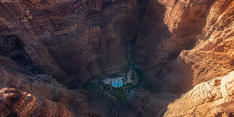 A luxury resort at the bottom of a deep canyon, dwarfed by layered rock walls rising on all sides, seen from above.