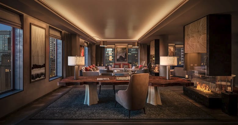 Aman New York penthouse living room at dusk with a lit fireplace, live-edge stone table, and Midtown Manhattan skyline through the windows