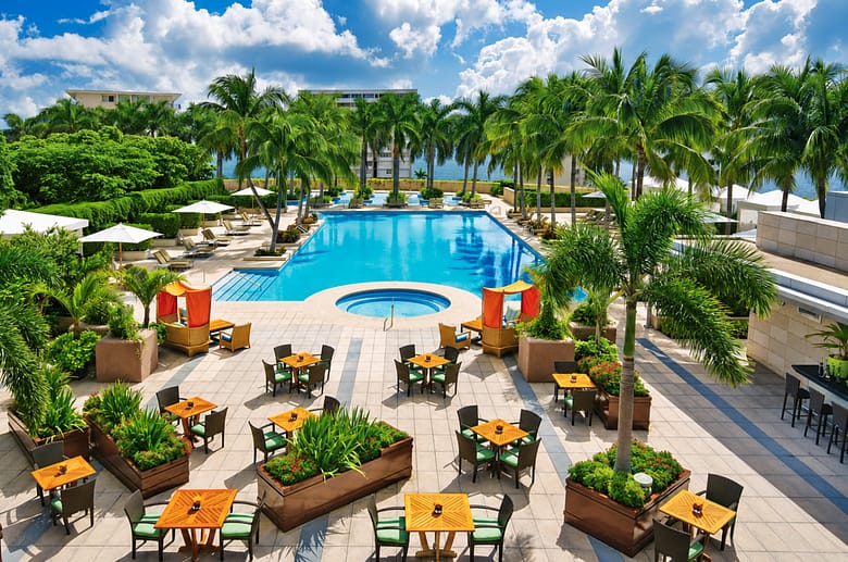 Two-acre pool terrace at Four Seasons Hotel Miami in Brickell, with palm trees, orange cabanas, and dining tables surrounding the pool above Biscayne Bay