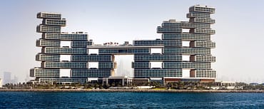 Luxury waterfront hotel with stacked modern towers rising above the shoreline and open sea in the foreground.