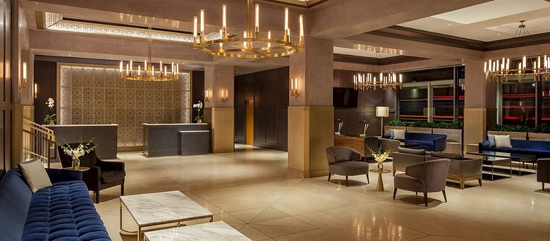 Luxury hotel lobby with high ceilings, brass chandeliers, marble tables, plush seating, and a contemporary reception area.