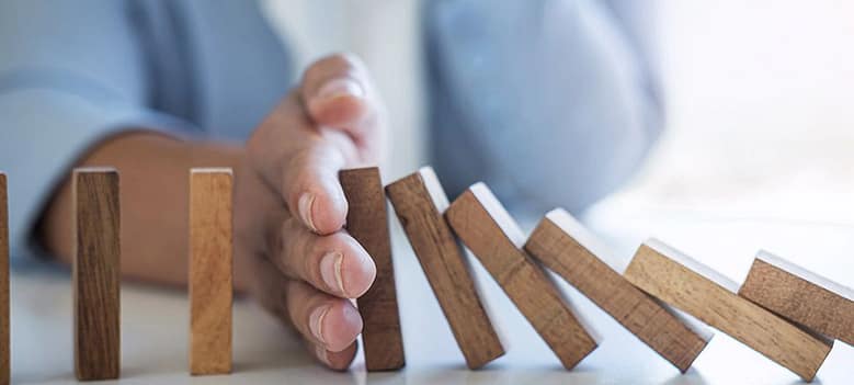 Hand stopping falling dominoes representing control of chain reactions and outcomes