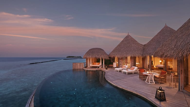 Luxury overwater villa resort at sunset with private infinity pool overlooking the ocean.