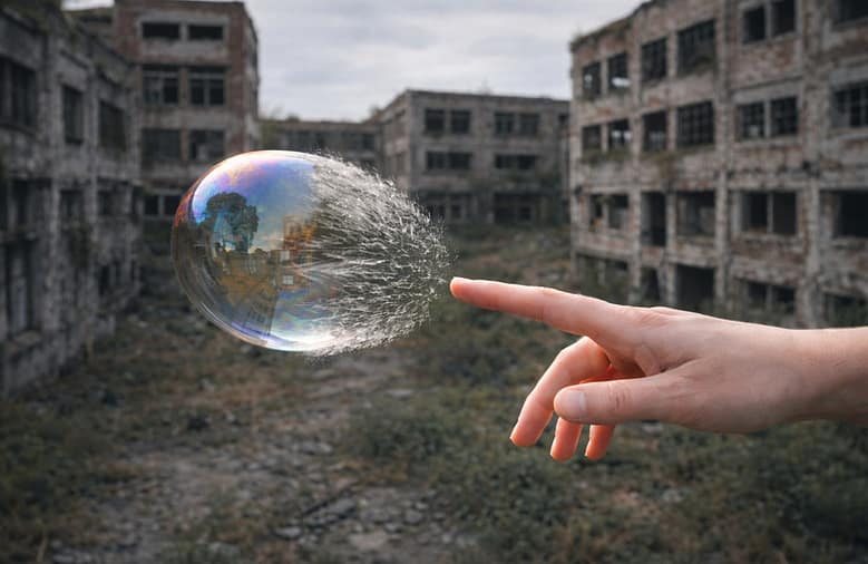 A soap bubble bursting on contact with a finger, set against abandoned industrial ruins — fragility behind a polished surface.