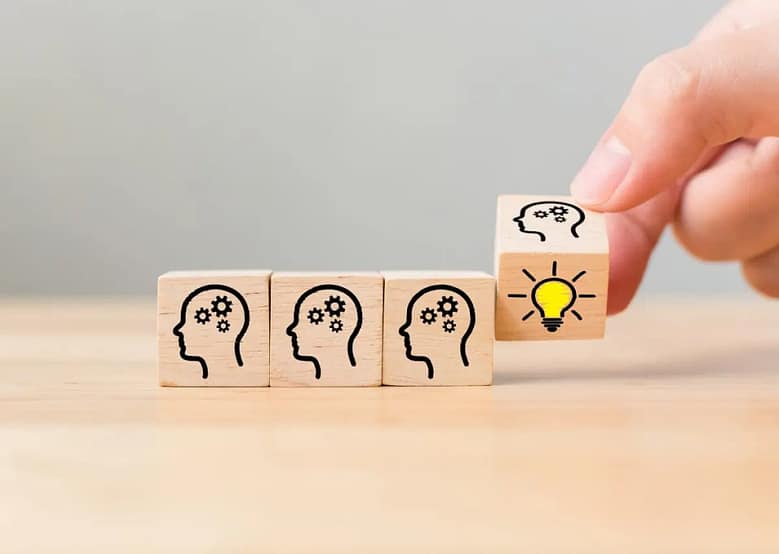 Knowledge formation concept illustrated with wooden blocks showing human head icons and a lightbulb idea being added to the sequence.