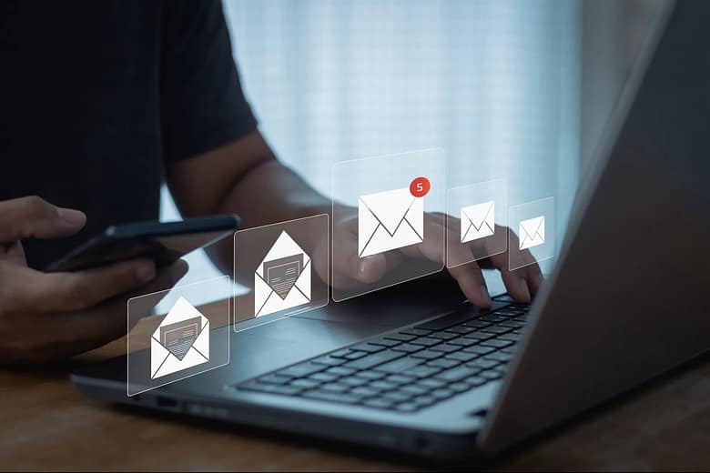 Hotel email marketing automation concept showing a traveler using a laptop and smartphone while multiple email notifications appear, representing lifecycle email communication and digital guest engagement.
