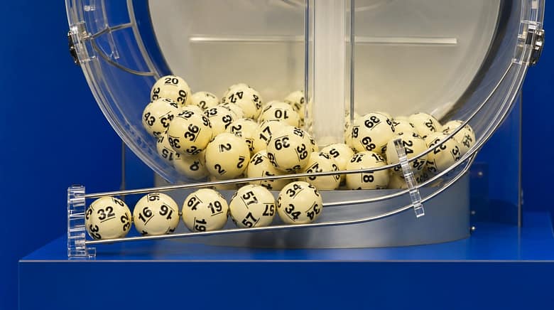 Powerball lottery balls in a drawing machine, numbered yellow balls lined up and ready for selection.