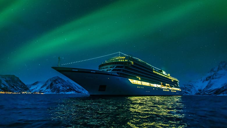 Aerial night view of a luxury cruise ship illuminated against dark water, illustrating the repositioning problem in luxury cruise demand architecture.