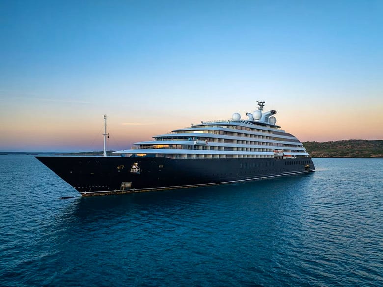 Luxury cruise ship sailing on calm blue water at sunset beneath a clear pastel sky